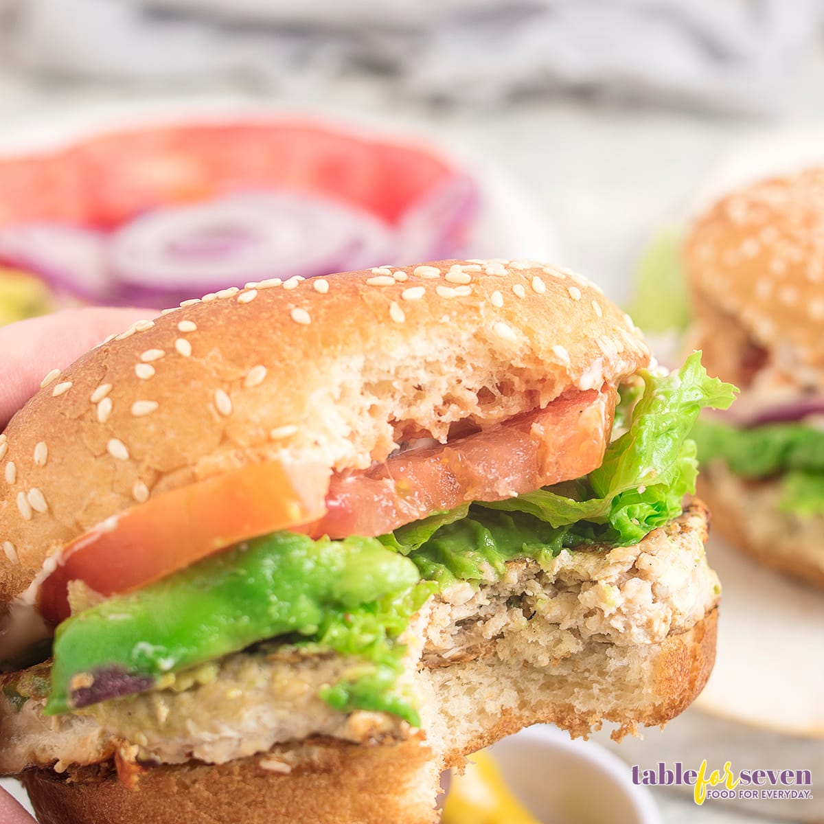 Partially eaten turkey burger with avocado and tomato slices