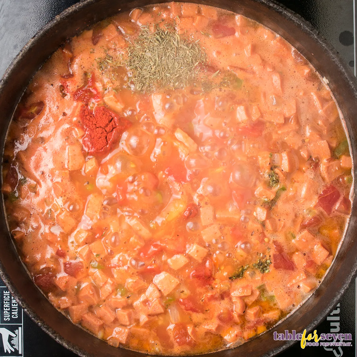 Bubbling gumbo with spices and herbs being mixed
