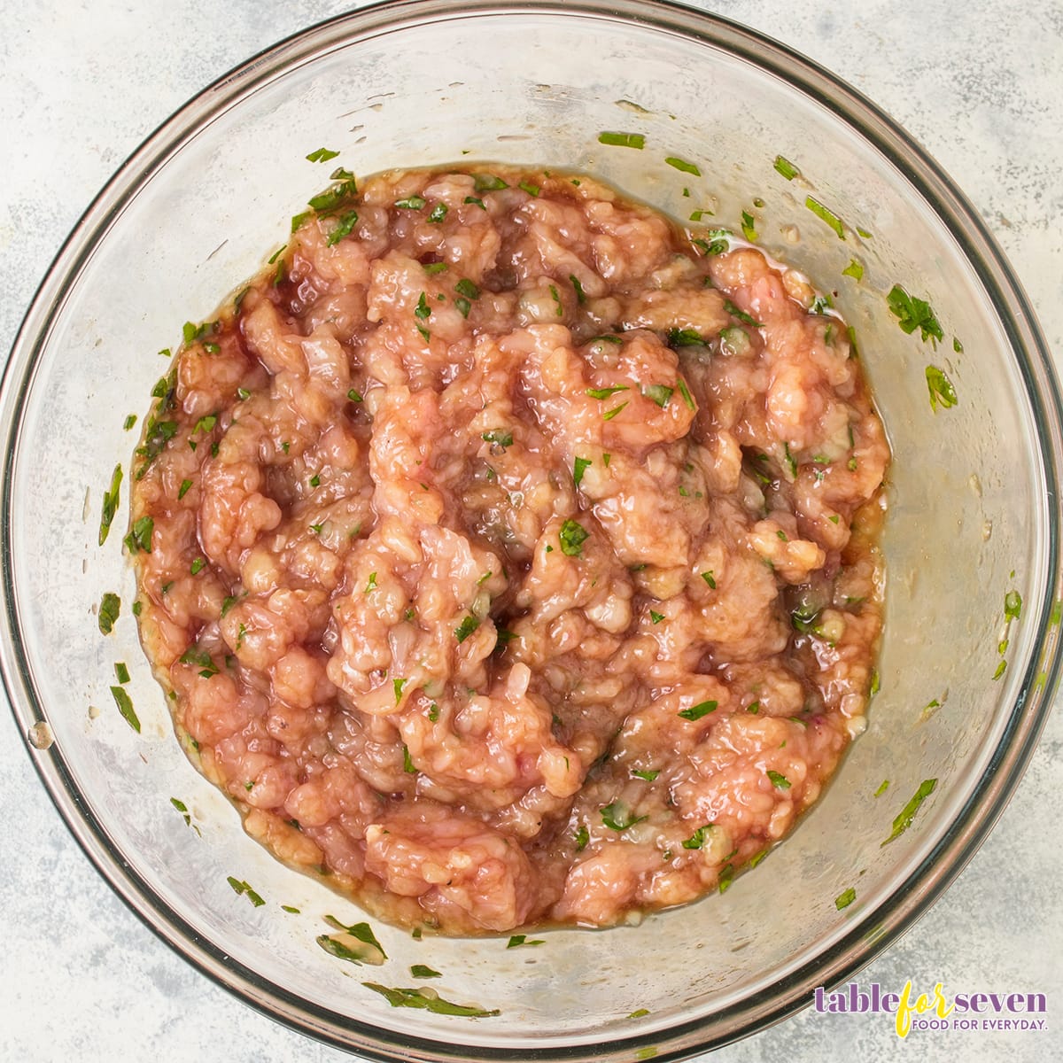 Ground turkey mixture with herbs and seasoning in a glass bowl