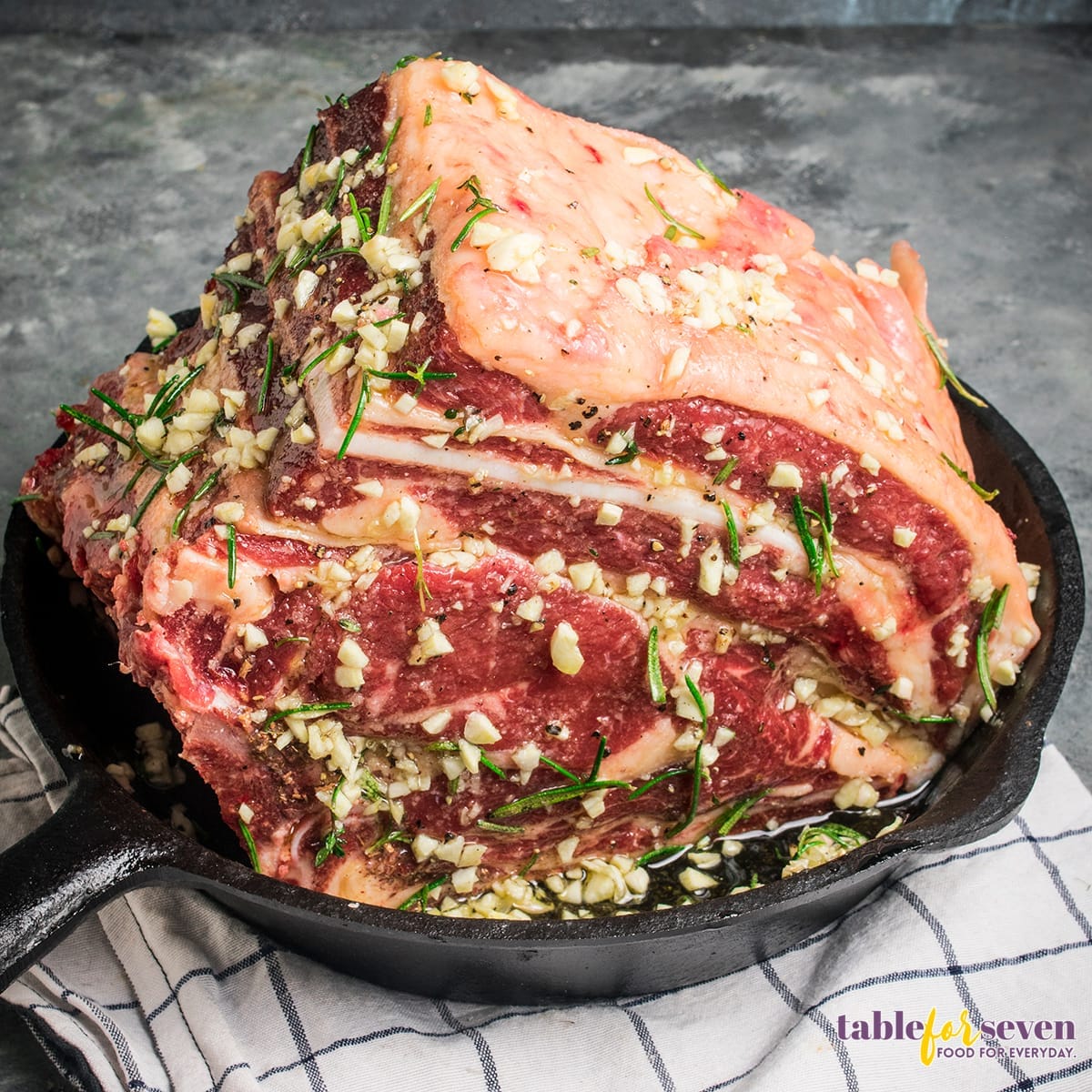 Raw prime rib seasoned with garlic and herbs in a skillet