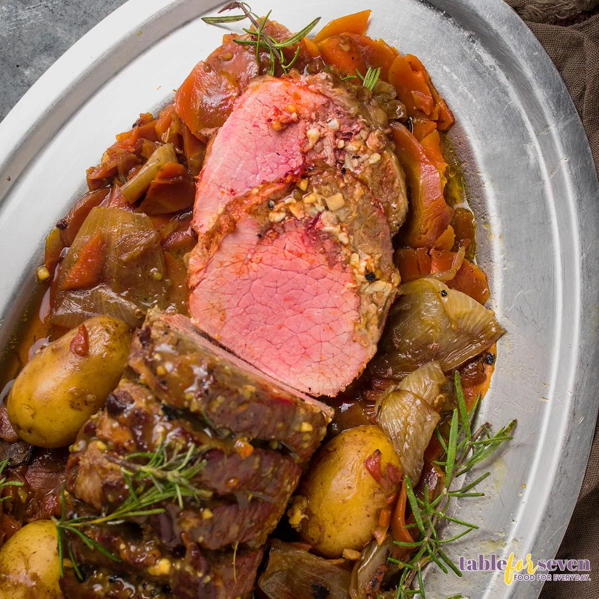 Rump roast served on a platter with vegetables and rosemary sprigs