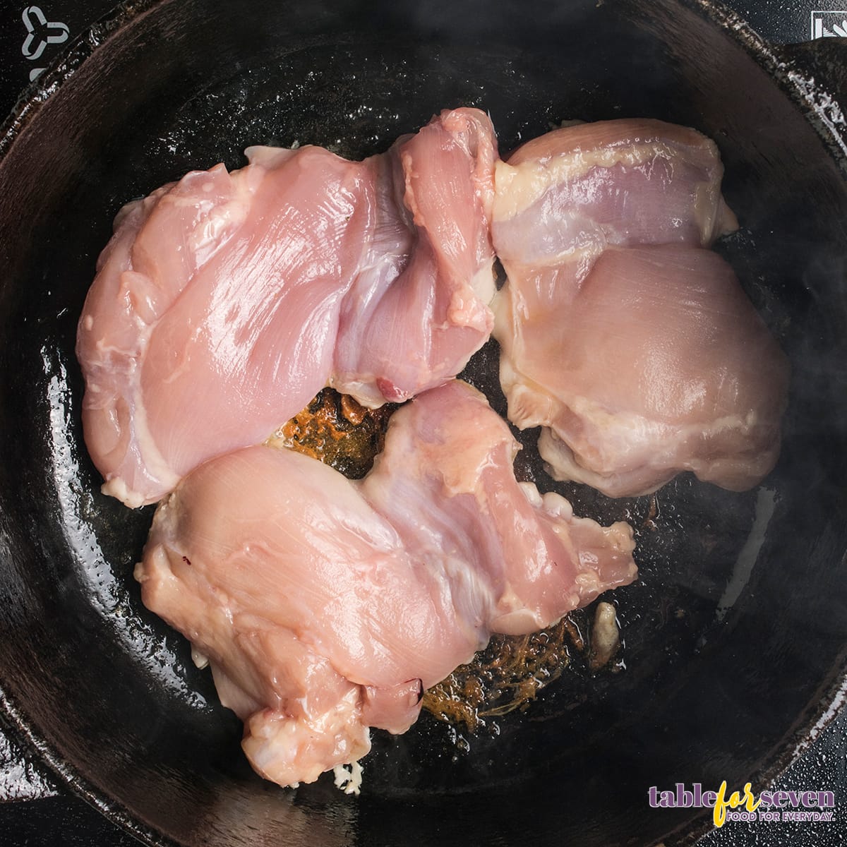 Raw chicken thighs searing in a hot skillet for Chicken Cacciatore recipe