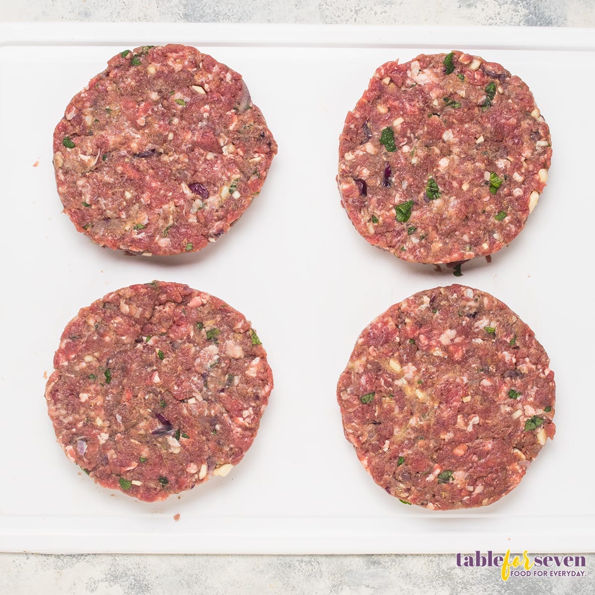 Four uncooked Gordon Ramsay Lamb Burger patties on a white cutting board