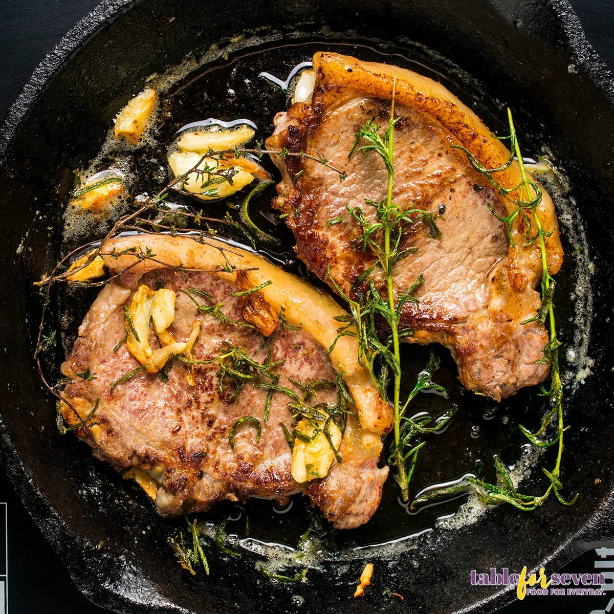 Steak cooking in a skillet with garlic and herbs